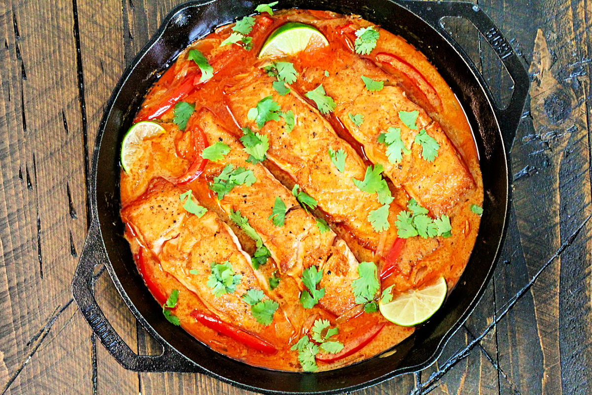 Thai salmon curry in a cast iron skillet on a wooden board