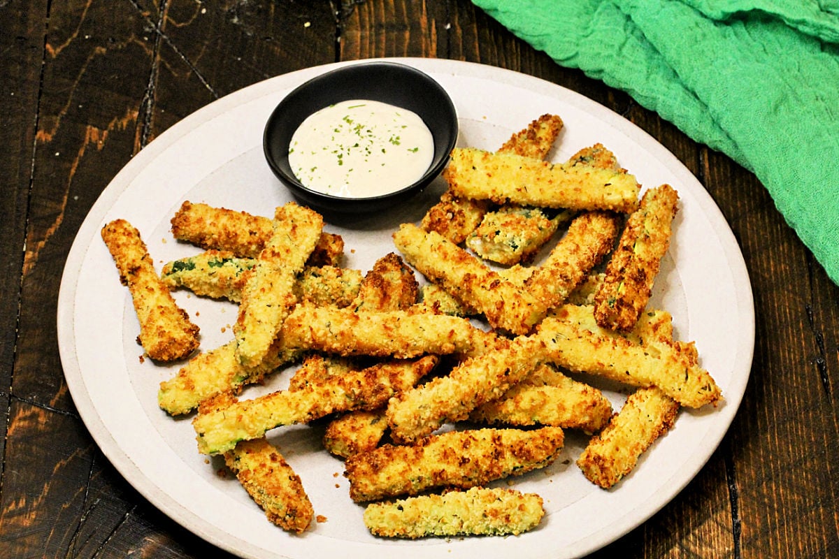 Air fryer zucchini fries on a plate with bowl of ranch dipping sauce and a green napkin.