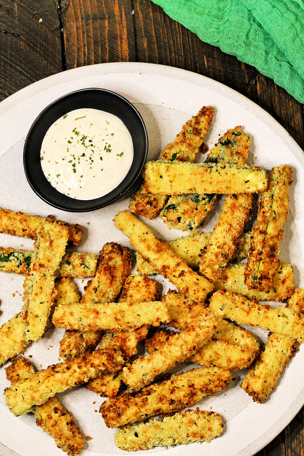 Air fryer zucchini fries on a plate with bowl of ranch dipping sauce and a green napkin.