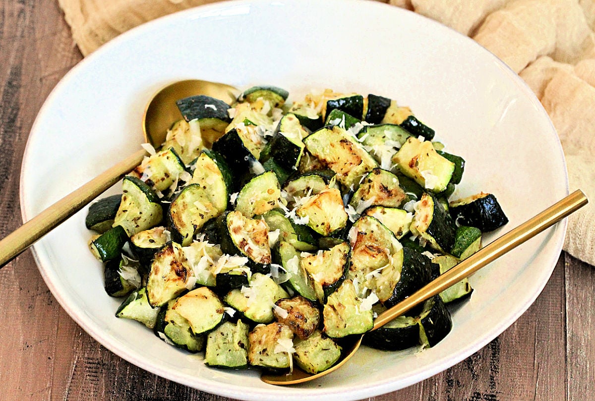 Horizontal image of zucchini in a white bowl with two gold spoons.