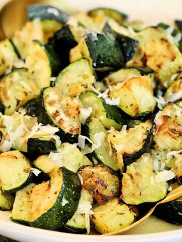 Air fryer zucchini in a white bowl with grated parmesan cheese on top.