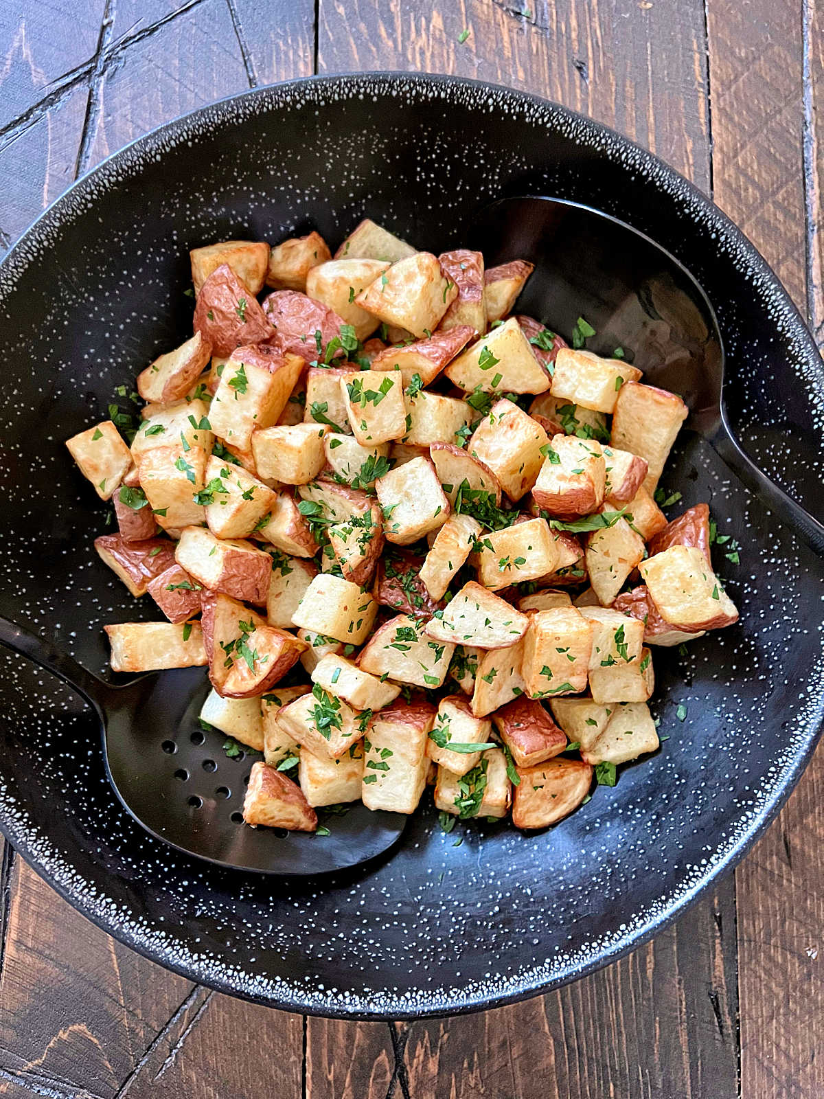 Air fryer diced potatoes in a black bowl with two black spoons. 
