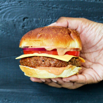 Holding a beyond burger with cheese, tomato and sauce.