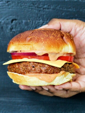 Holding a beyond burger with cheese, tomato and sauce.