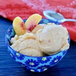 Two scoops of healthy peach frozen yogurt and two peach slices in a blue bowl.