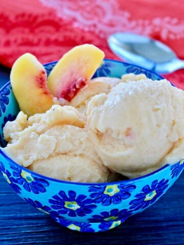 Two scoops of healthy peach frozen yogurt and two peach slices in a blue bowl.