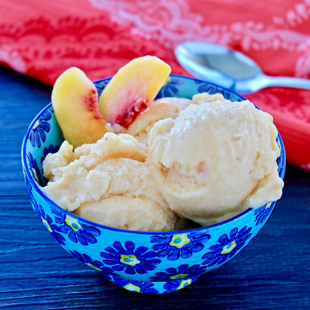 Two scoops of healthy peach frozen yogurt and two peach slices in a blue bowl.
