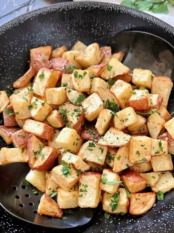 Air fryer diced potatoes in a black bowl with two black spoons.