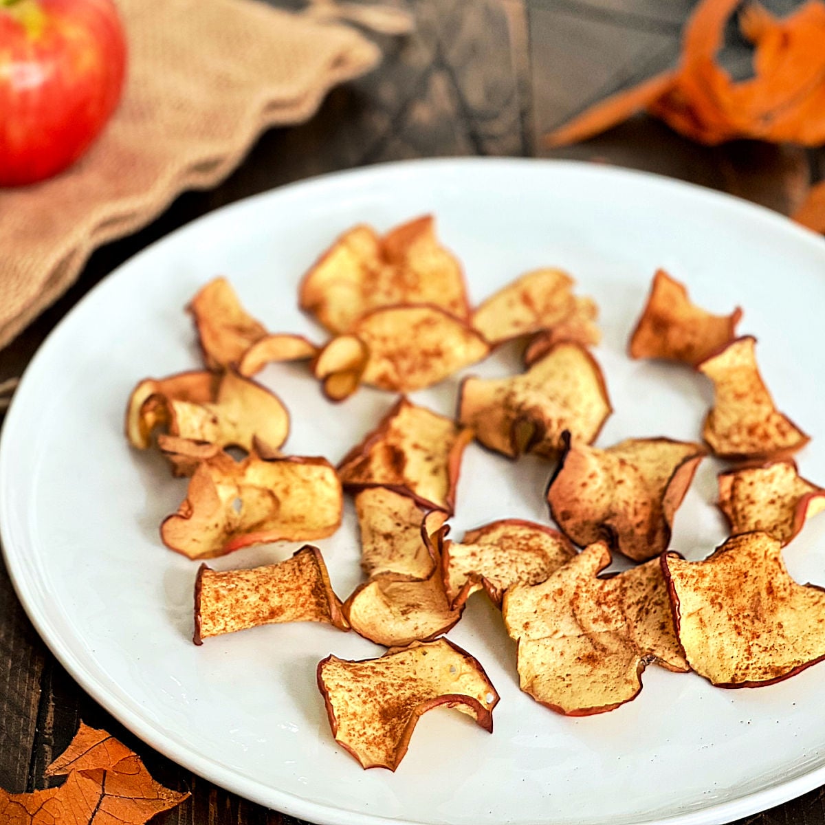 Air fryer apple chips on a white plate with an apple in the background.