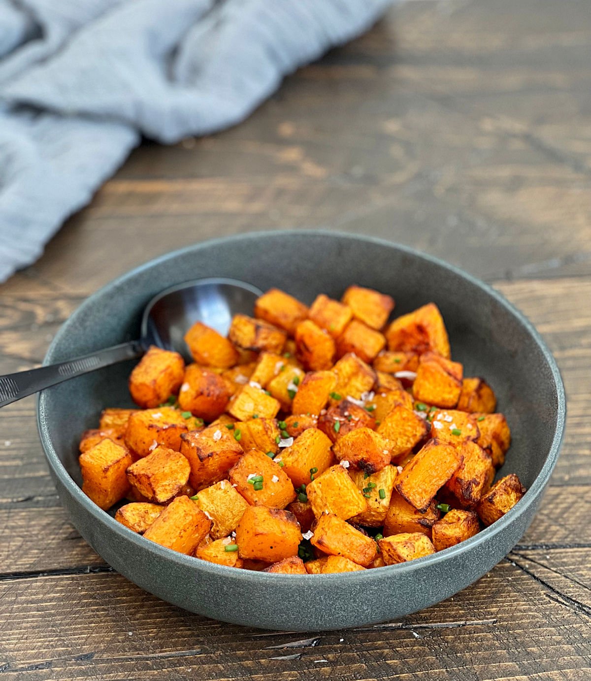 Air fryer butternut squash in a gray bowl on a wooden board with a gray napkin in the background.
