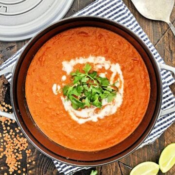 Overhead photo of red lentil coconut soup in a pot garnished with yogurt and cilantro.