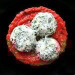 3 spinach gnudi on a black plate.