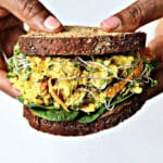 Two hands holding a chickpea egg salad sandwich.