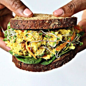 Two hands holding a chickpea egg salad sandwich.