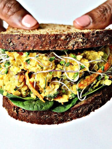 Two hands holding a chickpea egg salad sandwich.