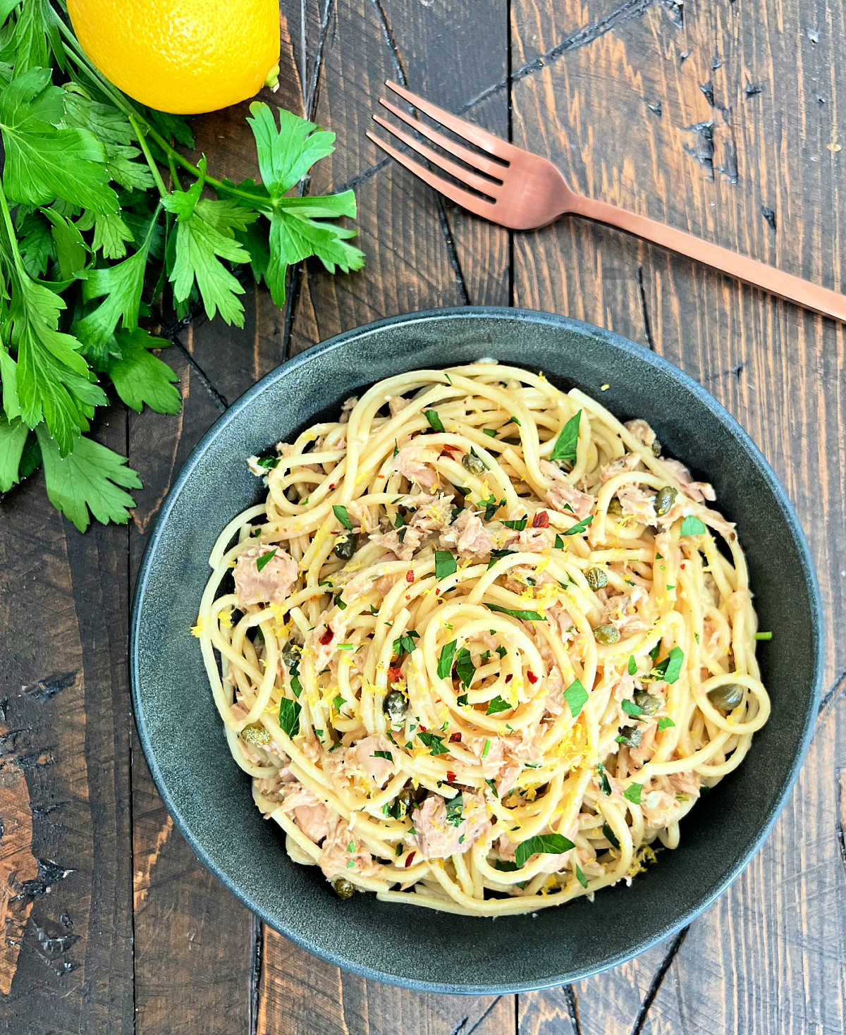 Overhead shot of tuna pasta in a dark gray bowl with a copper fork on the side.