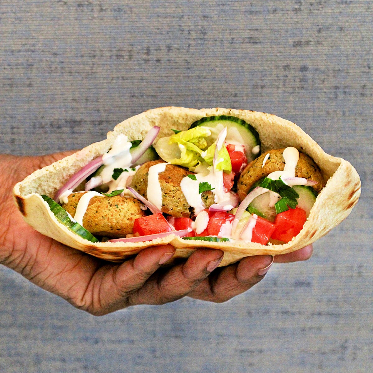 Close up of a falafel pita sandwich being held.