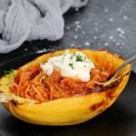 A spaghetti squash boat with tomato sauce and ricotta on a black plate.