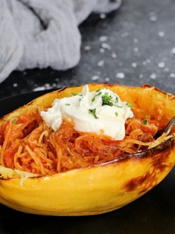 A spaghetti squash boat with tomato sauce and ricotta on a black plate.