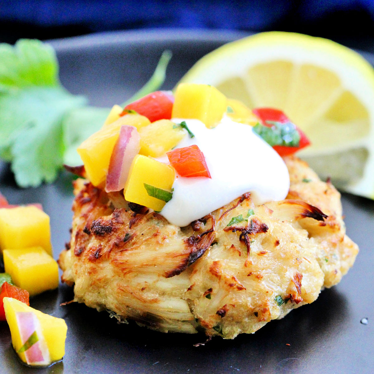 Close-up of a Maryland-style Old Bay crab cake with mango salsa on a black plate.