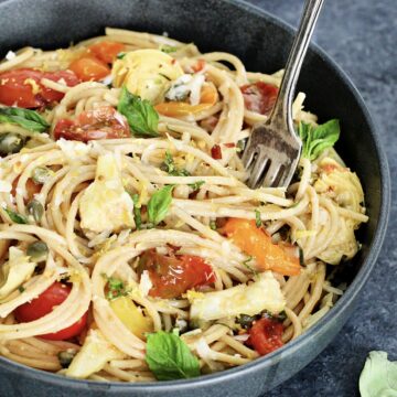 Close up of Mediterranean pasta in a gray bowl with a fork sticking in it.
