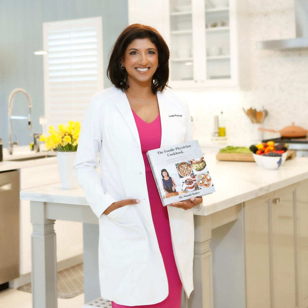 The Foodie Physician, Dr. Sonali Ruder in her kitchen holding her cookbook.