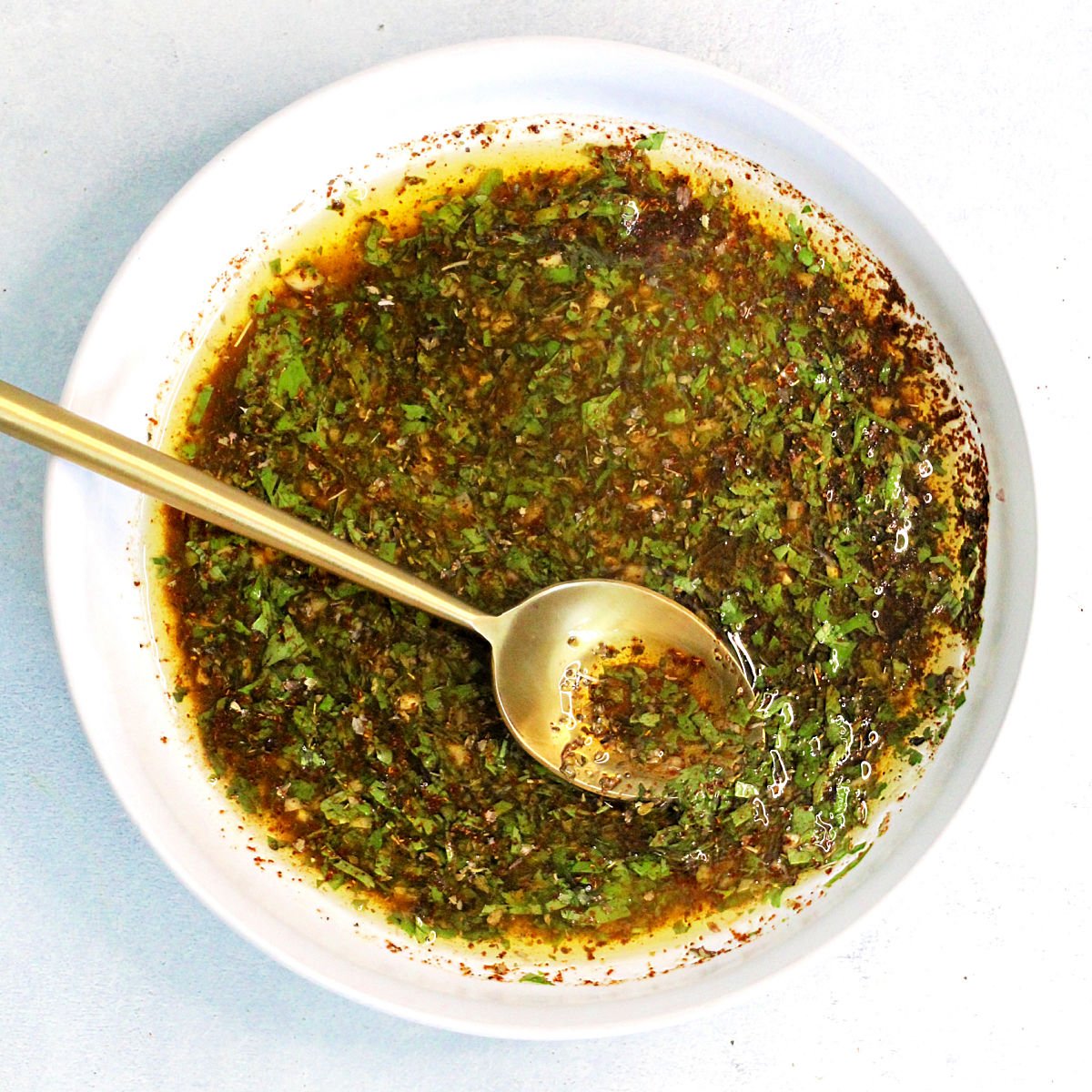 Marinade for chicken in a white bowl with a gold spoon.