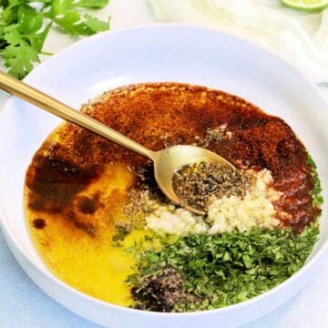 Mexican chicken marinade in white bowl with gold spoon.