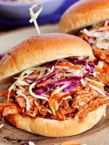 Two BBQ pulled chicken sandwiches on a wooden board.