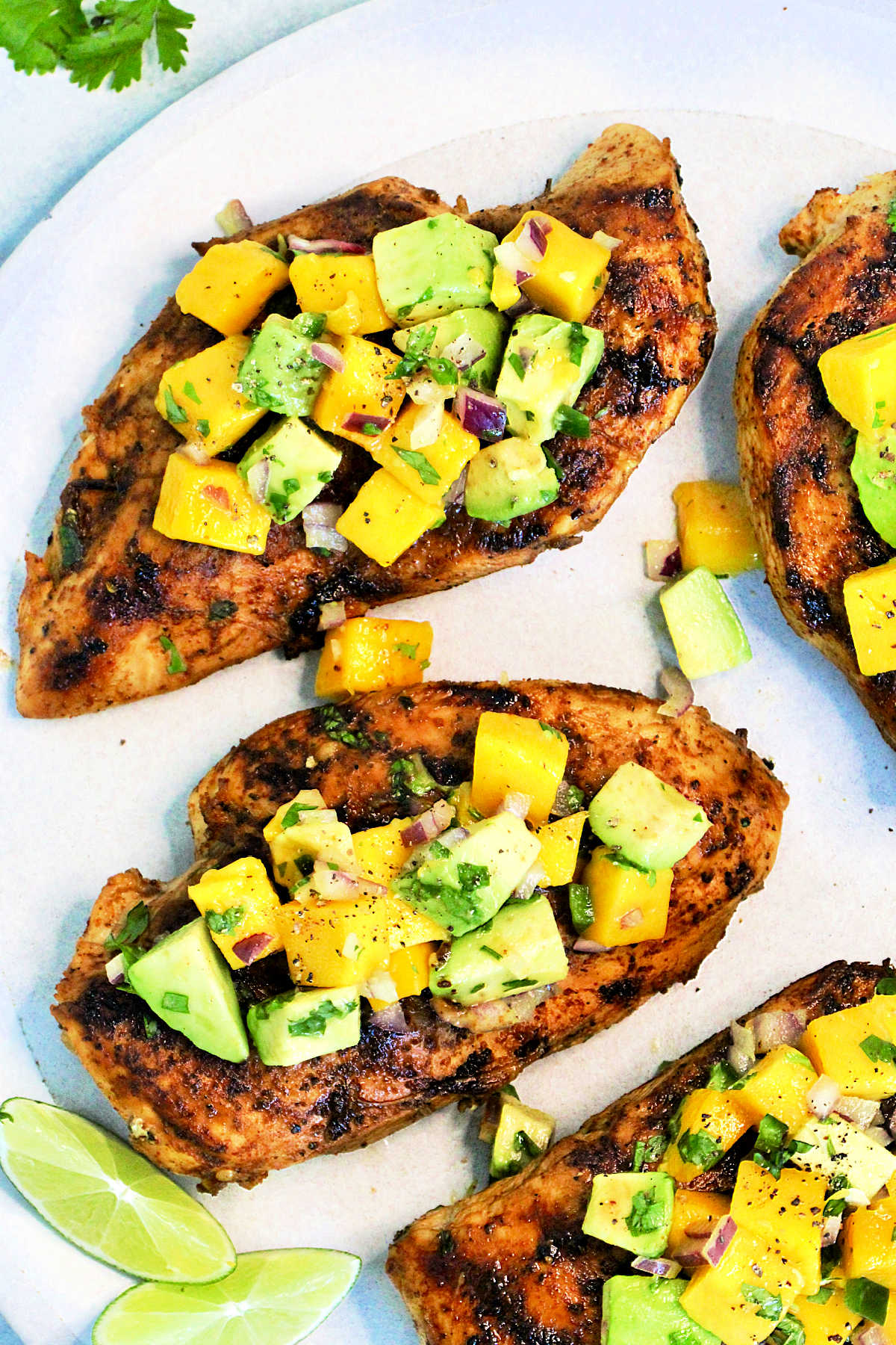 Overhead picture of grilled chicken with mango avocado salsa on a white plate.