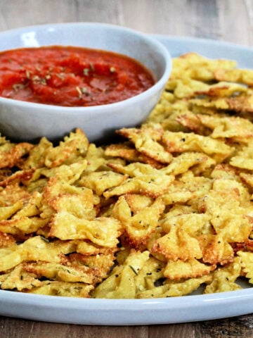 Pasta chips on a gray plate with a bowl of marinara.