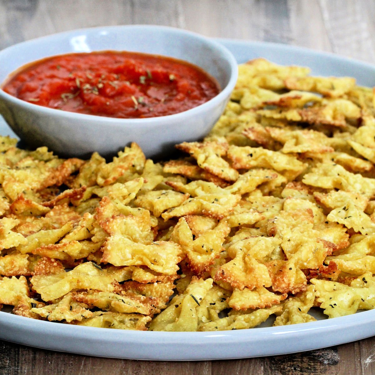 Pasta chips on a gray plate with a bowl of marinara.