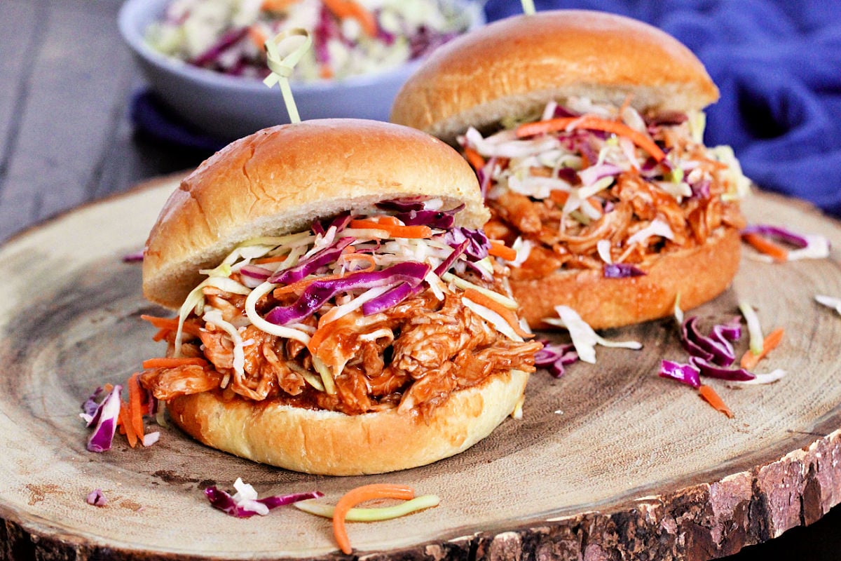 Two pulled chicken sandwiches on a wooden board. 