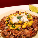 Pulled pork taco with corn salsa on a white plate.