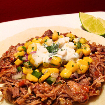 Pulled pork taco with corn salsa on a white plate.