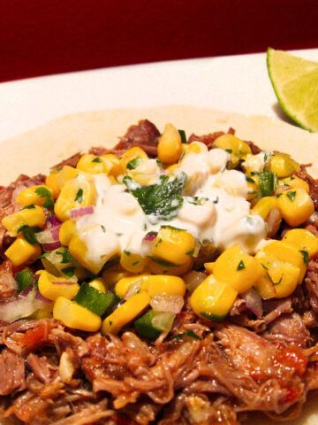 Pulled pork taco with corn salsa on a white plate.