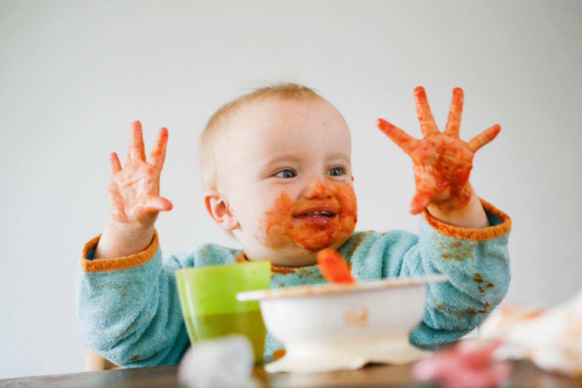 A messy baby with food on his face and hands