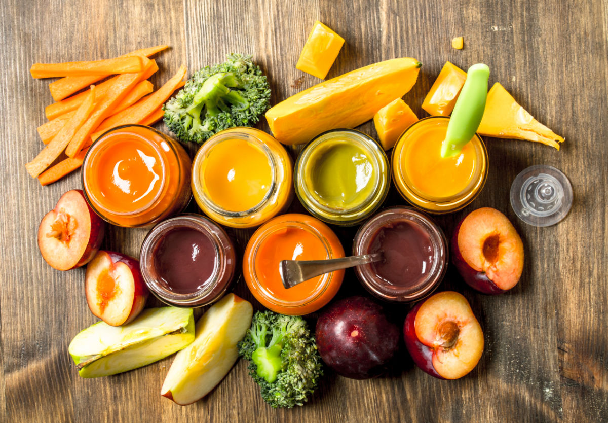 An assortment of jars with baby food surrounded by fruits and vegetables