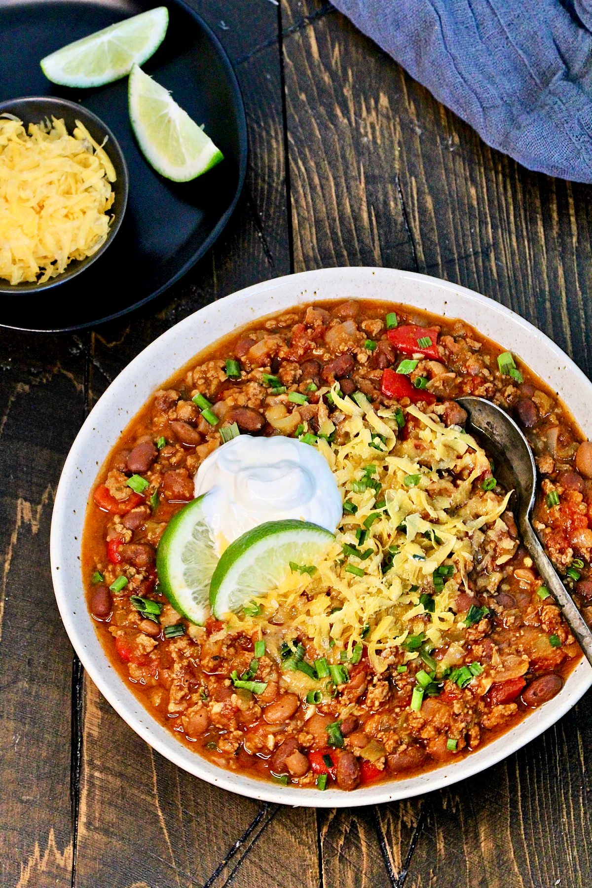 The Ultimate Turkey Chili garnished with cheese, sour cream and lime in a white speckled bowl.