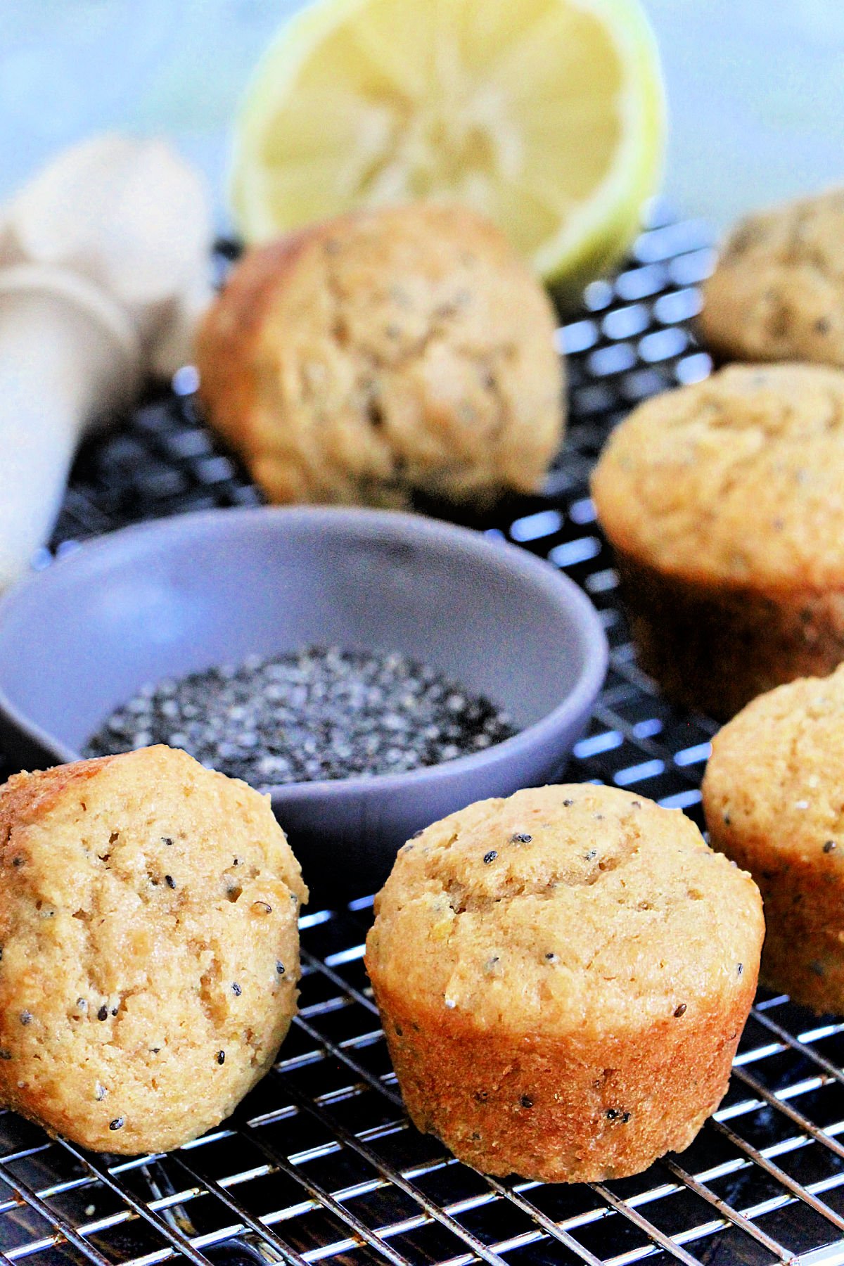 Lemon chia seed muffins on a baking rack with a bowl of chia seeds and a cut lemon