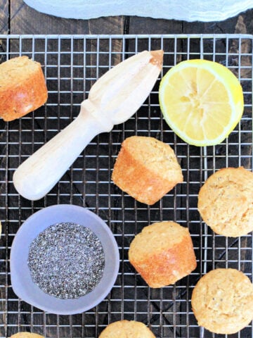 Lemon chia seed muffins on a baking rack with a bowl of chia seeds and a cut lemon.