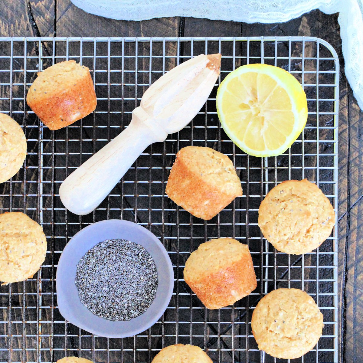 Lemon chia seed muffins on a baking rack with a bowl of chia seeds and a cut lemon.