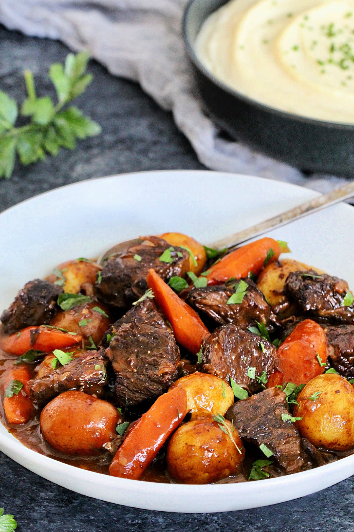 Classic Dutch Oven Beef Stew in a white bowl with a bowl of celery root puree nearby.