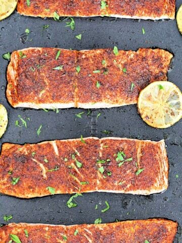 Four fillets of Low Sodium Chile Lime Salmon on a black baking sheet with limes slices around them.