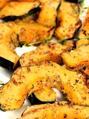 Slices of air fryer acorn squash garnished with fresh thyme on a white platter.