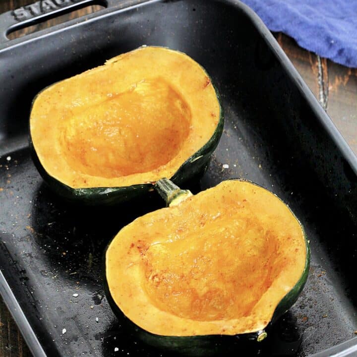 Microwaved acorn squash in a black baking dish with a blue napkin nearby.