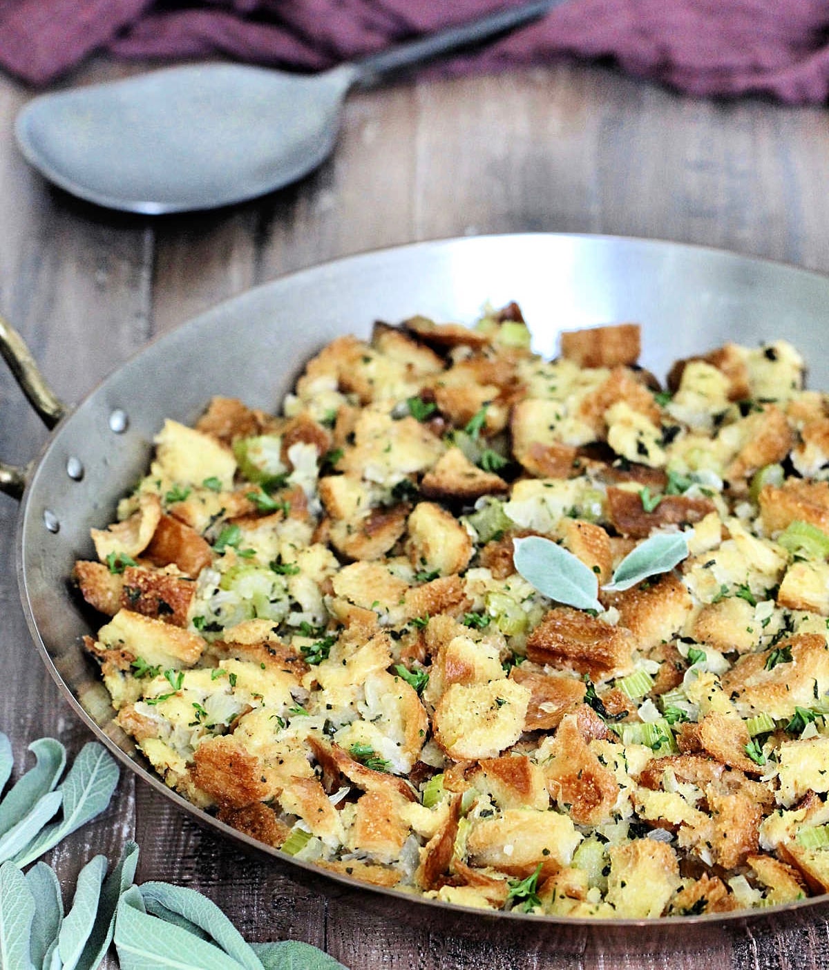 Classic Sage Stuffing in a copper pan with sage, a metal spoon and a brown napkin around it.