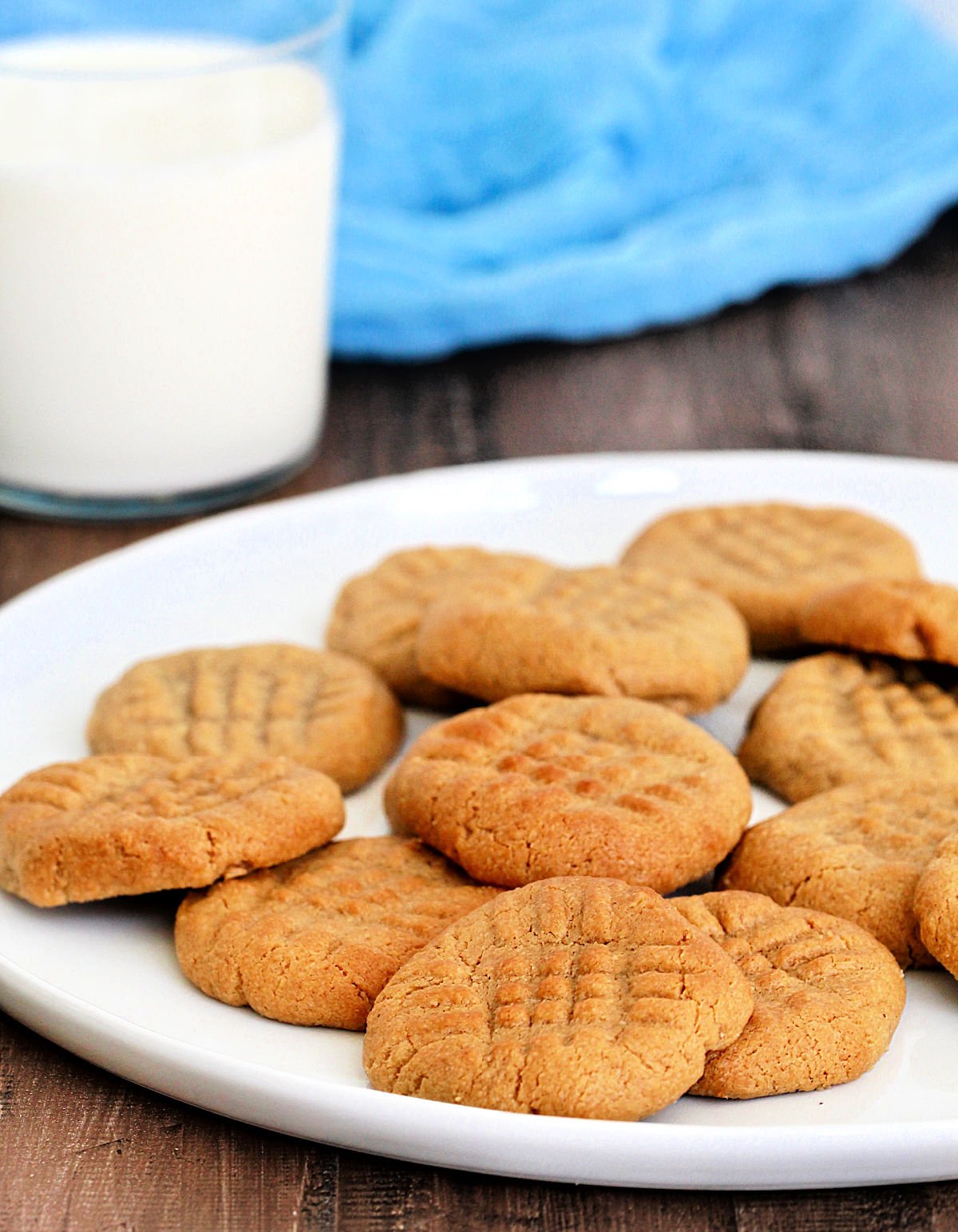 A plate of air fryer peanut butter cookies near a glass of milk and a blue napkin.
