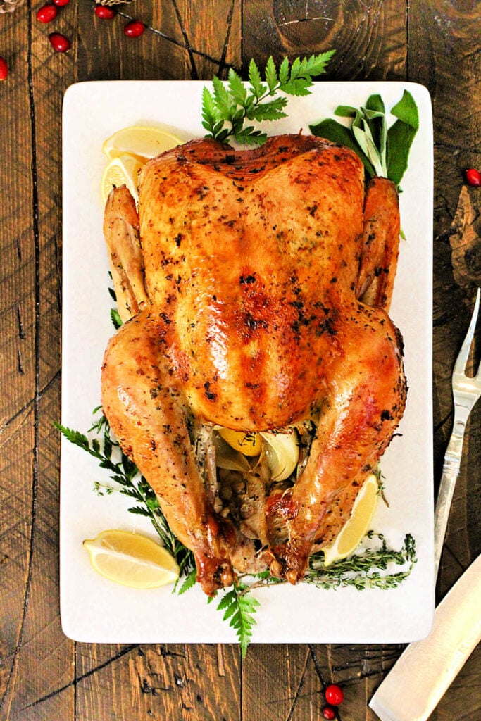 A holiday turkey on a white platter with rosemary and lemons around it