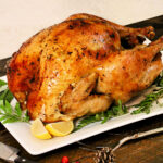 A holiday turkey on a white platter with rosemary and lemons around it
